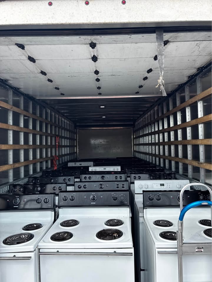 A truckload of white coil-top stoves being delivered to the lot